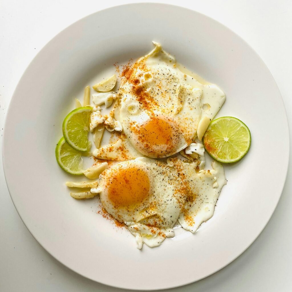 Delicious fried eggs with lime slices and spices on a ceramic plate, top view.